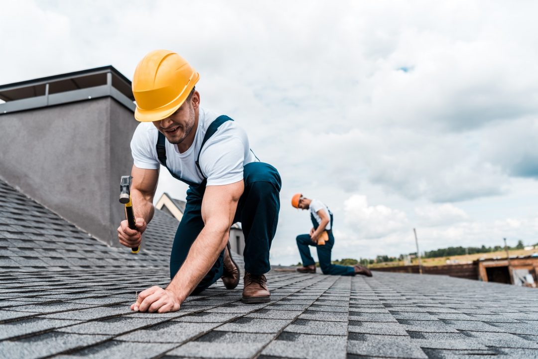 selective focus of handyman holding hammer while repairing roof near coworker.jpg